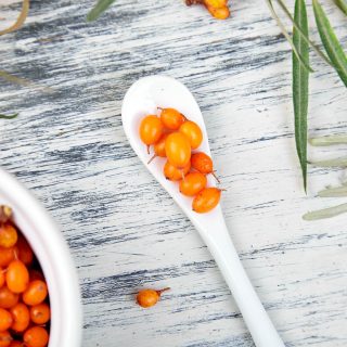 Natural, organic sea buckthorn berry in bowl and a on white wooden background. Branch of sea buckthorn. Top view.